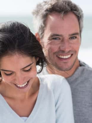 Portrait of a middle-aged couple having fun on the beach, they are wearing sweaters and the man has gray hair