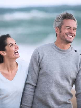 Portrait of a  couple walking on the beach, they are wearing sweaters and the man has gray hair