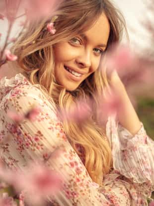 Portrait of amazing and beautiful young woman at spring in orchard of apricot trees in blossom. She is cheerful and happy, enjoying springtime.