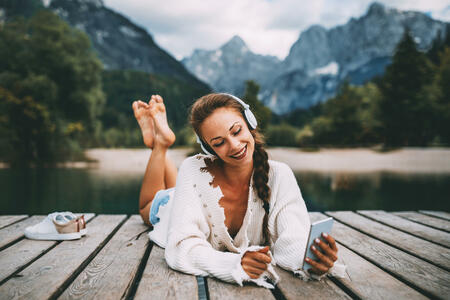 Attractive young woman listening to music via wifi headphones and smartphone on the lake