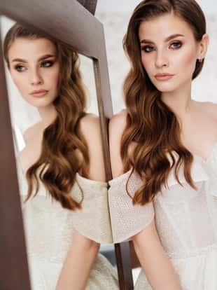 beautiful young woman with long hair, in a white dress is reflected in the mirror. the morning of the bride before the wedding. beautiful makeup