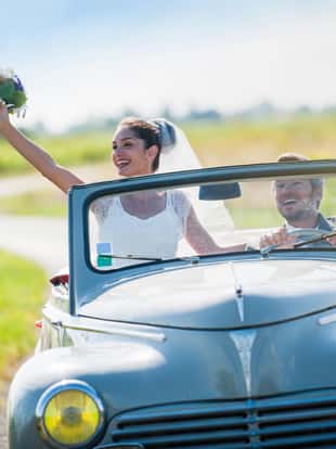 A newlywed couple is driving a retro car on a country road for their honeymoon