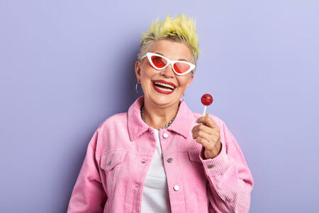 funny playfull cheerful old woman in pink stylish suit holding chup chups and posing to the camera. closeup portrait