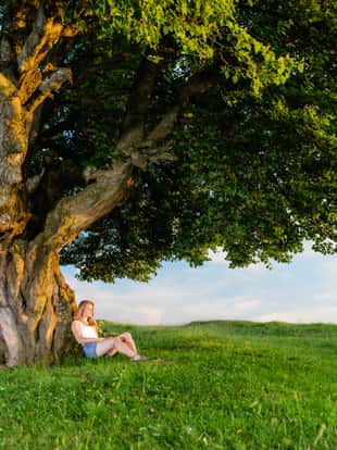 Young woman resting under a tree and meditating in a beautiful scenery
