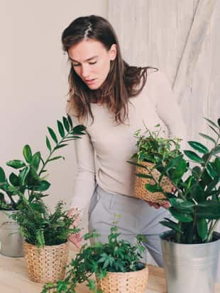 young woman watering flowerpots at home. Casual lifestyle series in modern scandinavian interior