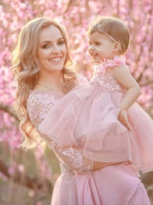 A woman in a dress like a pink bride in nature in the garden with a baby in her arms.