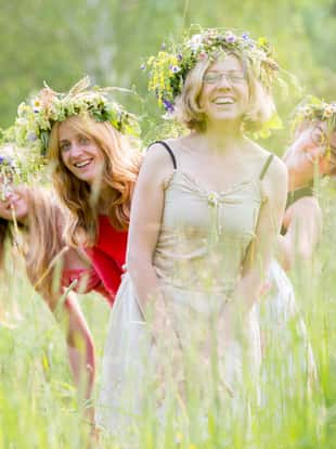 four happy women wearing wreaths on a meadow