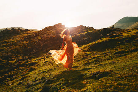 Beautiful model woman run in fashion dress on nature background in sunlight. Concept of Art, Travel, Bohemian Style, Freedom or Scenic Life. Velika Planina or Big Pasture Plateau, Slovenia, Europe.