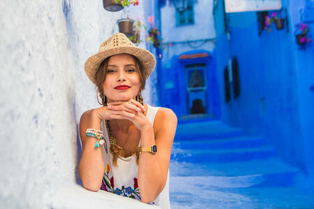 portrait of a young and beautiful woman with hat and white dress, looking to camera with smile and joy, visiting morocco