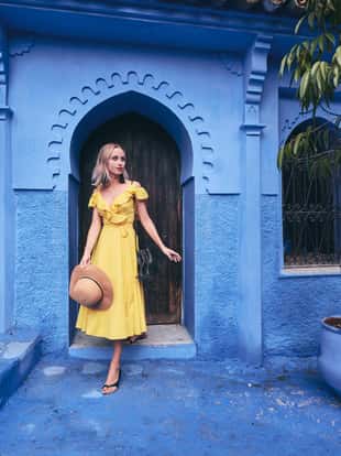 Colorful traveling by Morocco. Young woman in yellow dress walking in medina of blue city Chefchaouen.