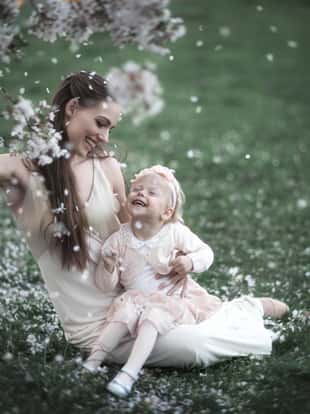 Mom holds her daughter on her lap and showers her with blossoming cherry petals.