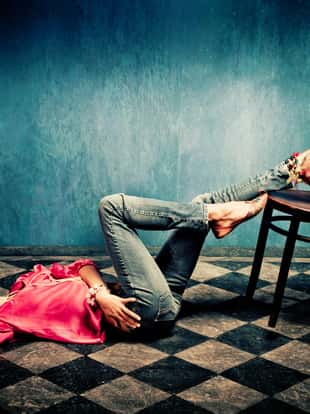young woman in oriental shirt and shoes lie on tiled floor, legs on chair, studio shot