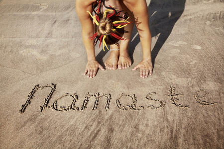 Woman doing yoga on the beach near Namaste handwriting in Goa, India