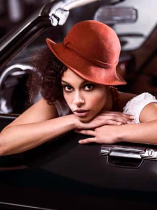 Fashionable Retro African-American young woman leaning on old timer car and looking at camera.