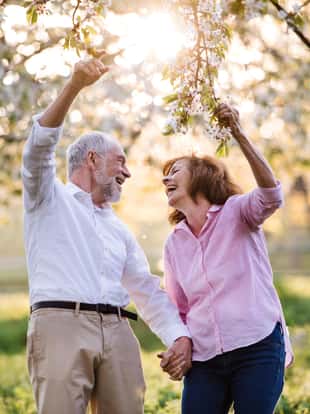 Beautiful senior couple in love on a walk outside in spring nature under blossoming trees, laughing.
