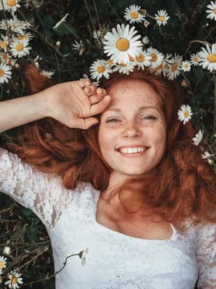 Beautiful young girl with curly red hair in chamomile field