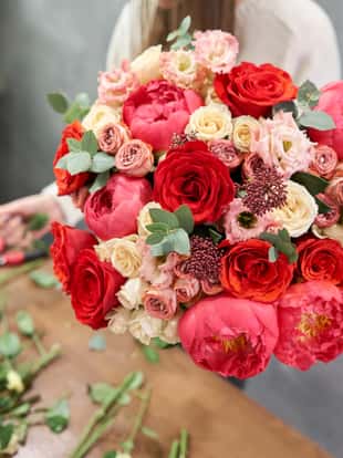 European floral shop concept. Florist woman creates red beautiful bouquet of mixed flowers. Handsome fresh bunch. Education, master class and floristry courses. Flowers delivery