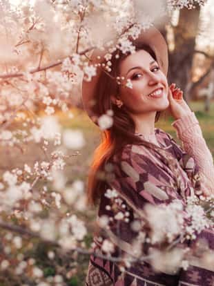 Happy middle-aged woman walking in spring blooming garden at sunset. Stylish spring outfit