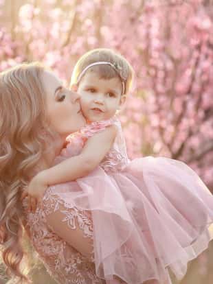 Portrait of young beautiful mother with her little girl. Close up still of loving family. Attractive woman holding her child in pink flowers and smiling.