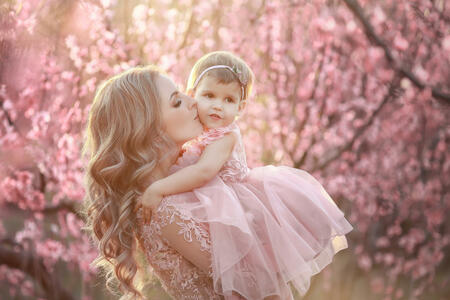 Portrait of young beautiful mother with her little girl. Close up still of loving family. Attractive woman holding her child in pink flowers and smiling.