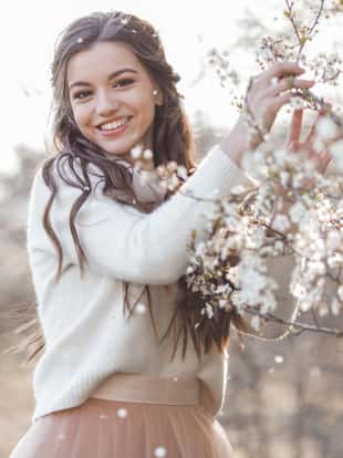 Beautiful smiling girl posing near blossom cherry tree with white flowers. Spring time, beauty concept