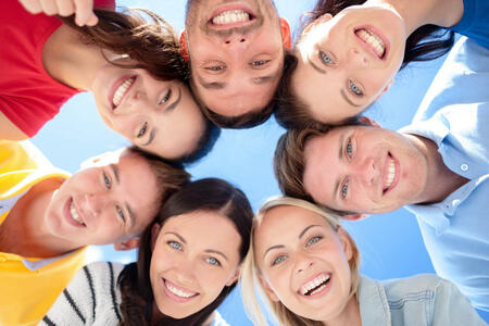 friendship, summer vacation, holidays and people concept - group of smiling friends standing in circle over blue sky