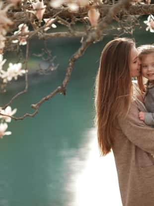 A woman holds a child in her arms against the background of a lake in a garden with magnolia.