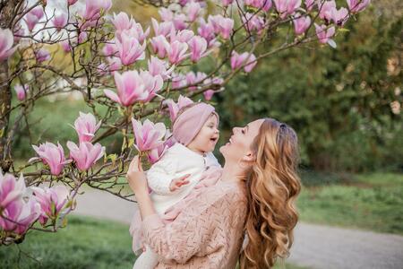 Beautiful young mother and little daughter near the magnolia. Spring family portrait. Blooming tree.