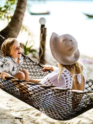 Happy little boy and his mother having fun while sitting on hammock at the beach in summer day.