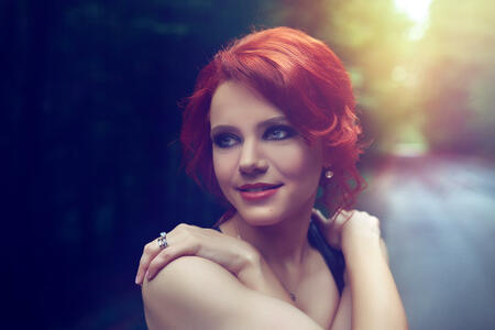 attractive red hair woman with makeup and hairstyle with arms crossed in the forest smiling.