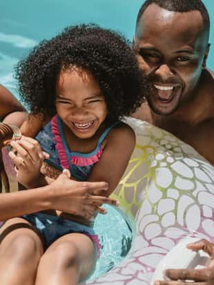 Man and woman playing with their daughter on inflatable ring in swimming pool. Family of three enjoying summer holidays in swimming pool.