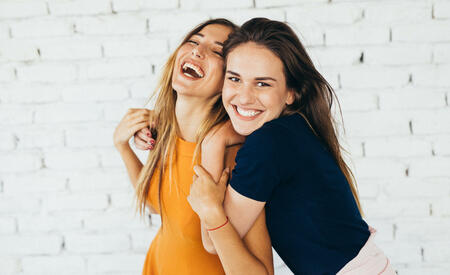 Two friends dancing and having fun in front of a white brick wall.