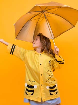 happy joyful girl in a beautiful yellow raincoat in the image of a bee holds a silver umbrella and extends her hand on a yellow background.