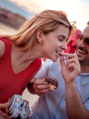 Happy young couple having fun outdoors,eating donuts.