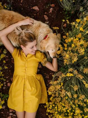 Photo of a young woman and her dog lying in the immortelle field on a beautiful sunny day; beautiful and peaceful weekend getaway, far from the hustle of the city.