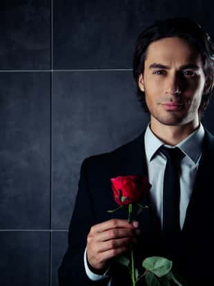 portrait of handsome romantic young man in formalwear holding red rose