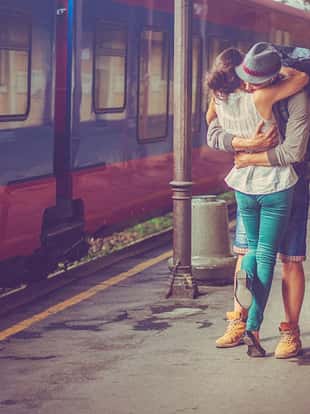 Close-up portrait of a happy woman and man at the railway platform, embracing and feeling in love. Romantic moment after a period of separation