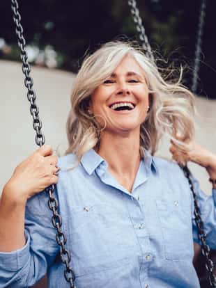 Smiling senior woman with gray hair sitting on swing, having fun and enjoying retirement