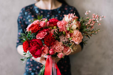 Very nice young woman holding beautiful blossoming flower bouquet of fresh roses, carnations, in passionate red colors on the grey background