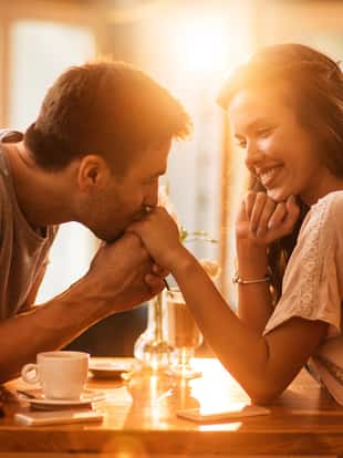 Smiling woman enjoying in a cafe while being kissed in a hand by her boyfriend.