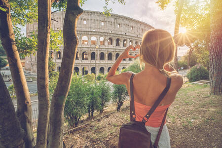Young woman at the Colosseum in Rome making a heart shape finger frame with hands loving travel in Italy