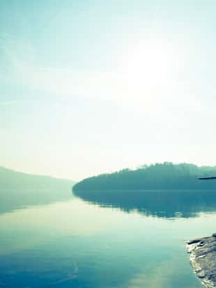 Woman sitting on the shore of the lake. Clear sunny day.