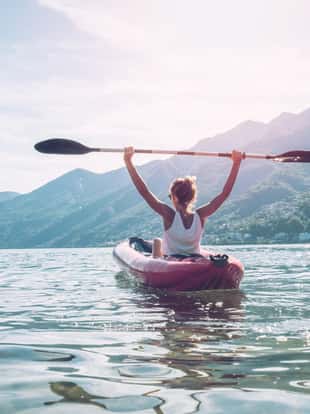 View of a young woman canoeing on beautiful mountain lake in Switzerland. Inflatable red canoe on water with mountain sceneryPeople travel outdoor activity concept