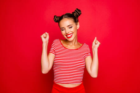 Portrait of happy cute young woman with toothy smile raised hands and celebrate achievement goal isolated on red background
