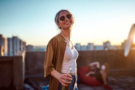 Woman dancing and holding bottle of beer at roof party.