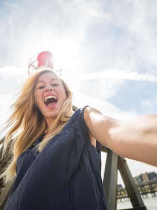Young woman taking a selfie at the Trouville lighthouse in Normandy-France. Summertime on the coast, sunlight passing through.