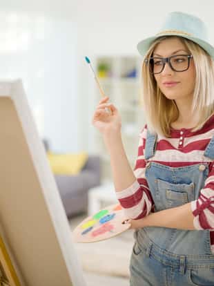 Young woman drawing on canvas and looking at the painting at home