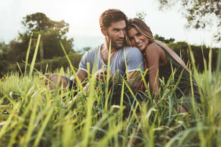 Shot of affectionate young couple enjoying a day outdoors. Man and woman sitting on grass field on a summer day.