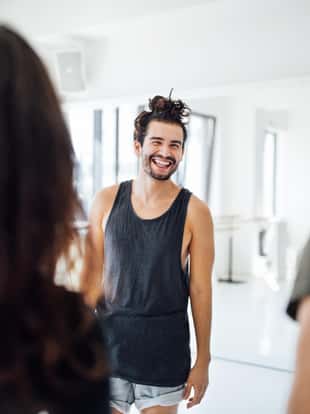 Cheerful man looking at friends in ballet studio. Young ballet dancers are standing at dance studio. They are wearing sportswear.