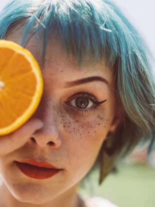 Beautiful young girl with dyed blue hair and red lipstick holding slice of orange